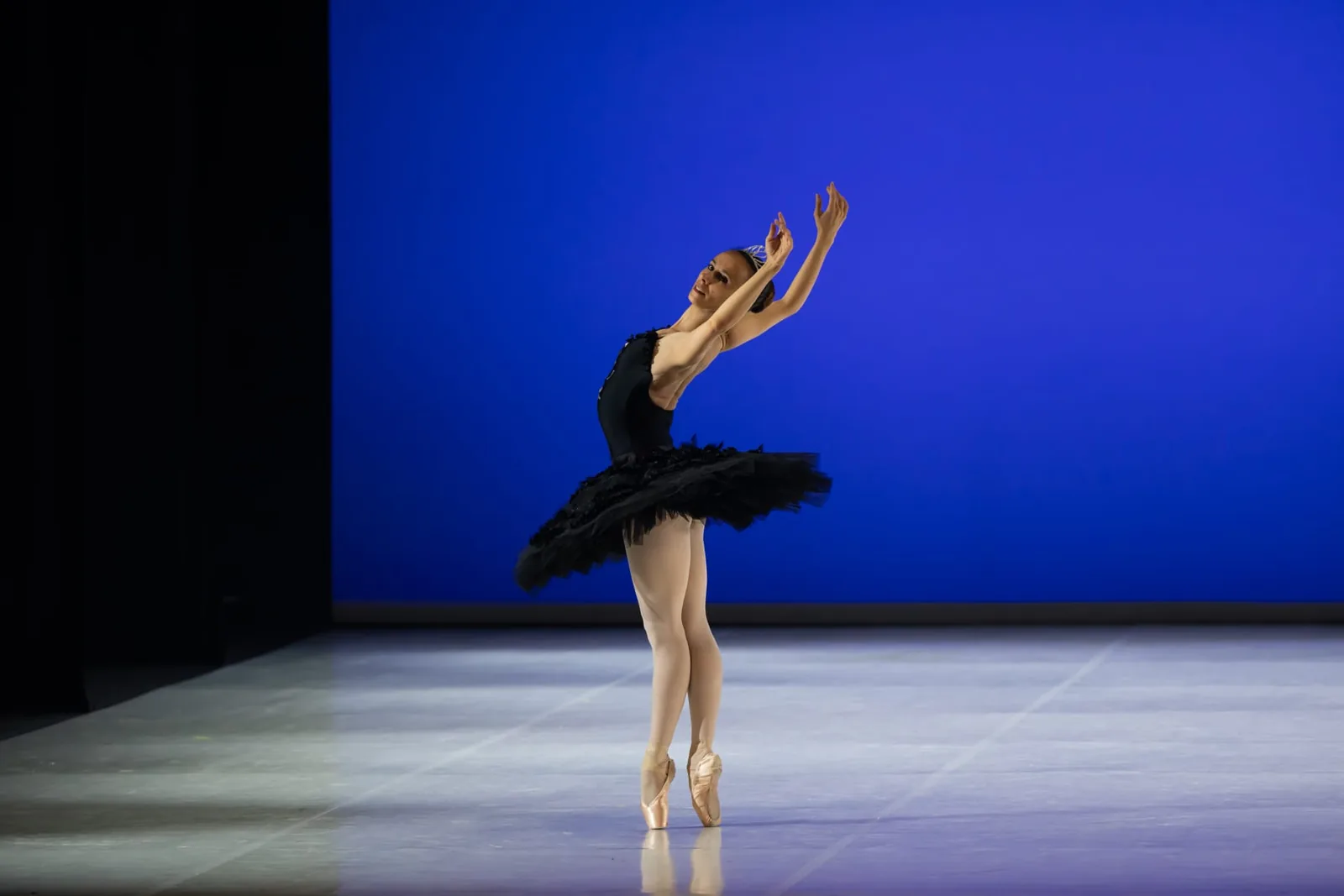 Arianna Ongarato sulle punte in tutù nero, braccia in quinta, su fondo blu di scena — Free Harmony Dance Time